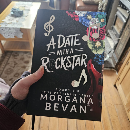 Book titled 'A Date with a Rockstar' by Morgana Bevan held in a hand with a living room background.