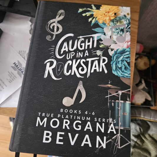 Book titled 'Caught Up in a Rockstar' by Morgana Bevan with musical notes and flowers on the cover.